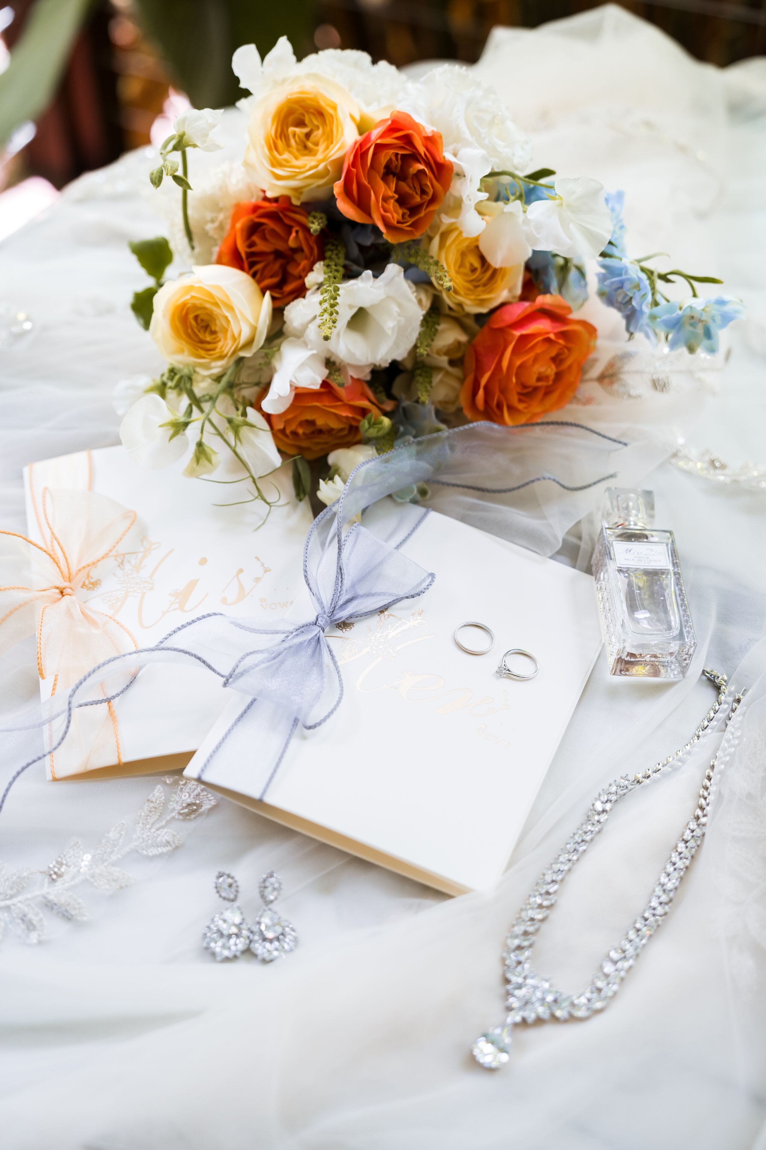 Un ramo de flores, una caja de regalo, una botella de perfume y joyas sobre una superficie blanca.