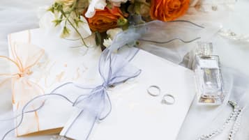 Un ramo de flores, una caja de regalo, una botella de perfume y joyas sobre una superficie blanca.