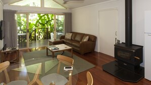 A spacious living room with a brown leather sofa, a glass coffee table, and a black wood-burning stove. - Songbirds Rainforest Retreat (Tamborine Mountain)