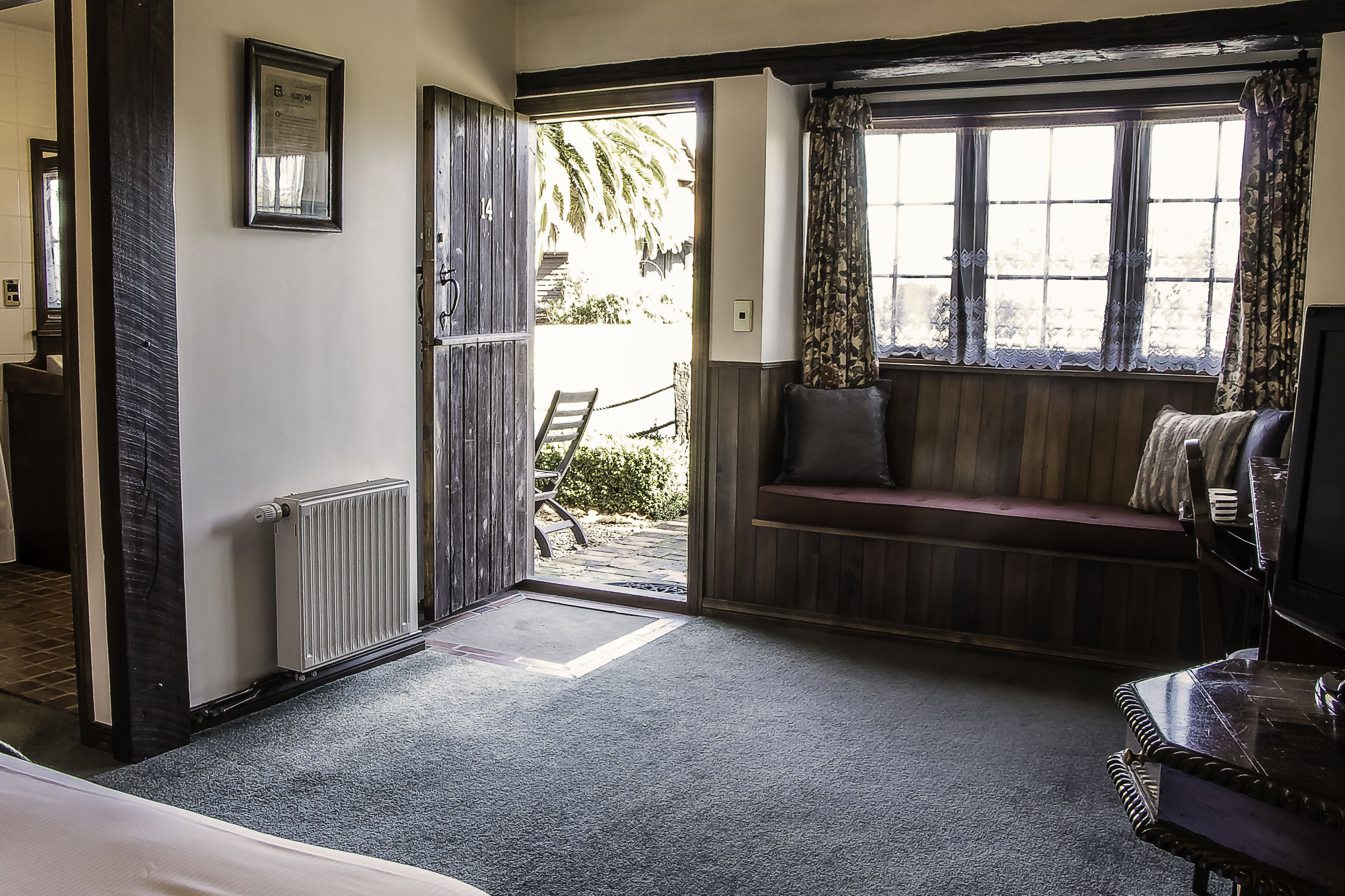 Een kamer met een houten bank bij een raam, een radiator en een deur naar buiten.
