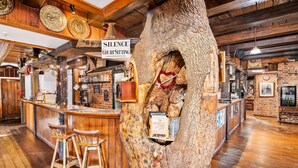 Un coin bar rustique avec un grand tronc d’arbre servant de pièce maîtresse, des tabourets de bar en bois et un panneau indiquant « Silence, zone de repos ».