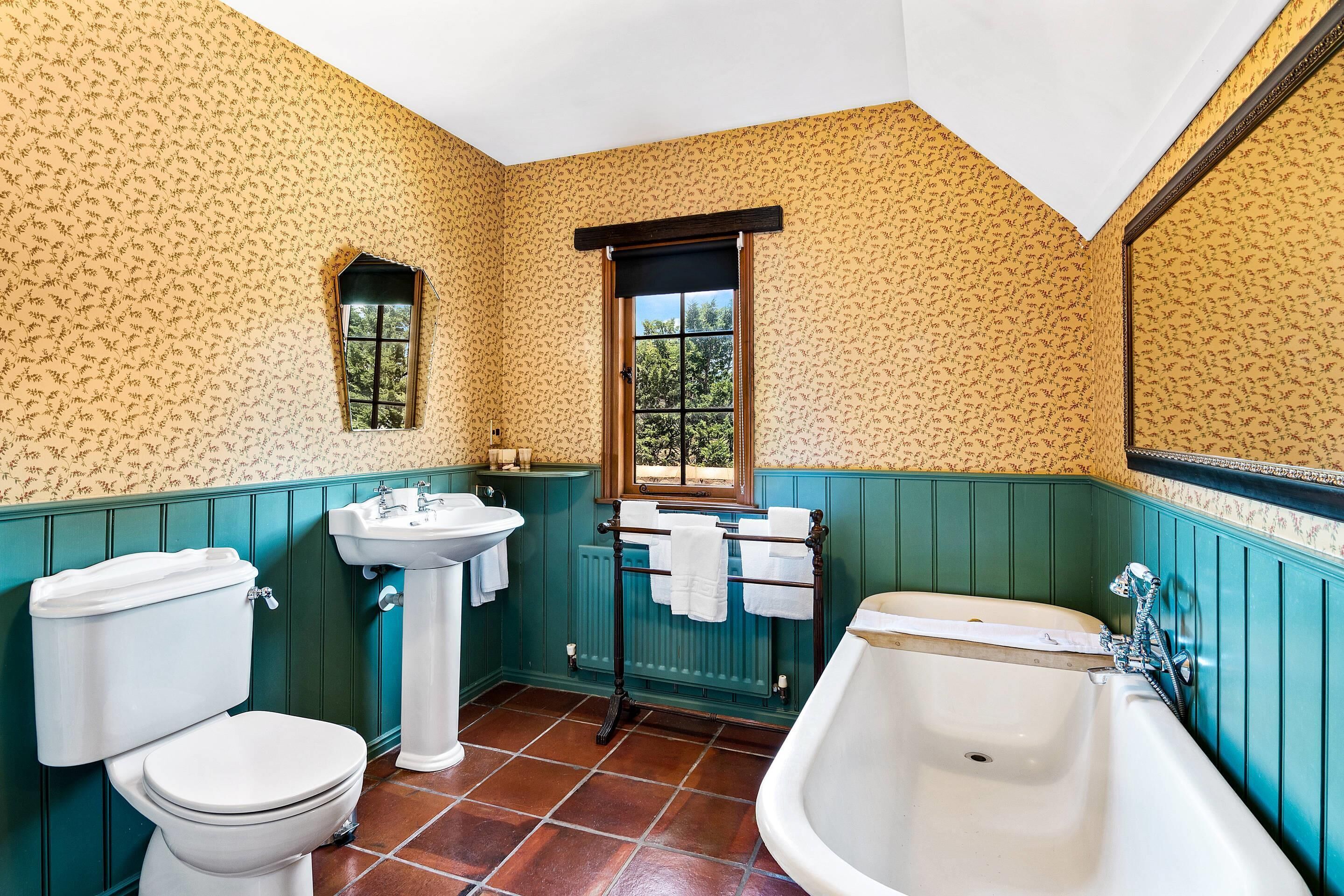 Un baño con inodoro, lavamanos y bañera, con papel tapiz estampado y paredes revestidas de paneles verdes.