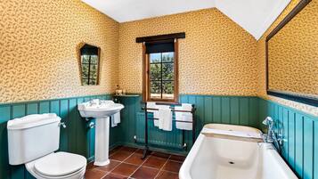 Un baño con inodoro, lavamanos y bañera, con papel tapiz estampado y paredes revestidas de paneles verdes.