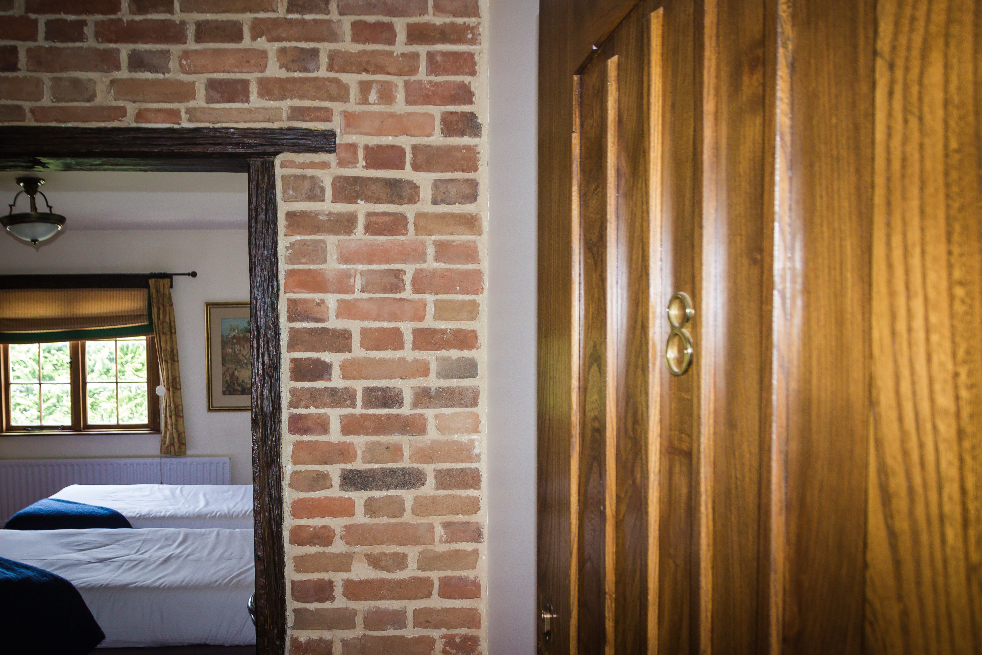 Una habitación con pared de ladrillo, puerta de madera y cama con ropa blanca.