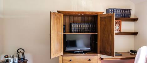 A compact room with a wooden cabinet containing books, a television, and a small table with cups and a kettle.