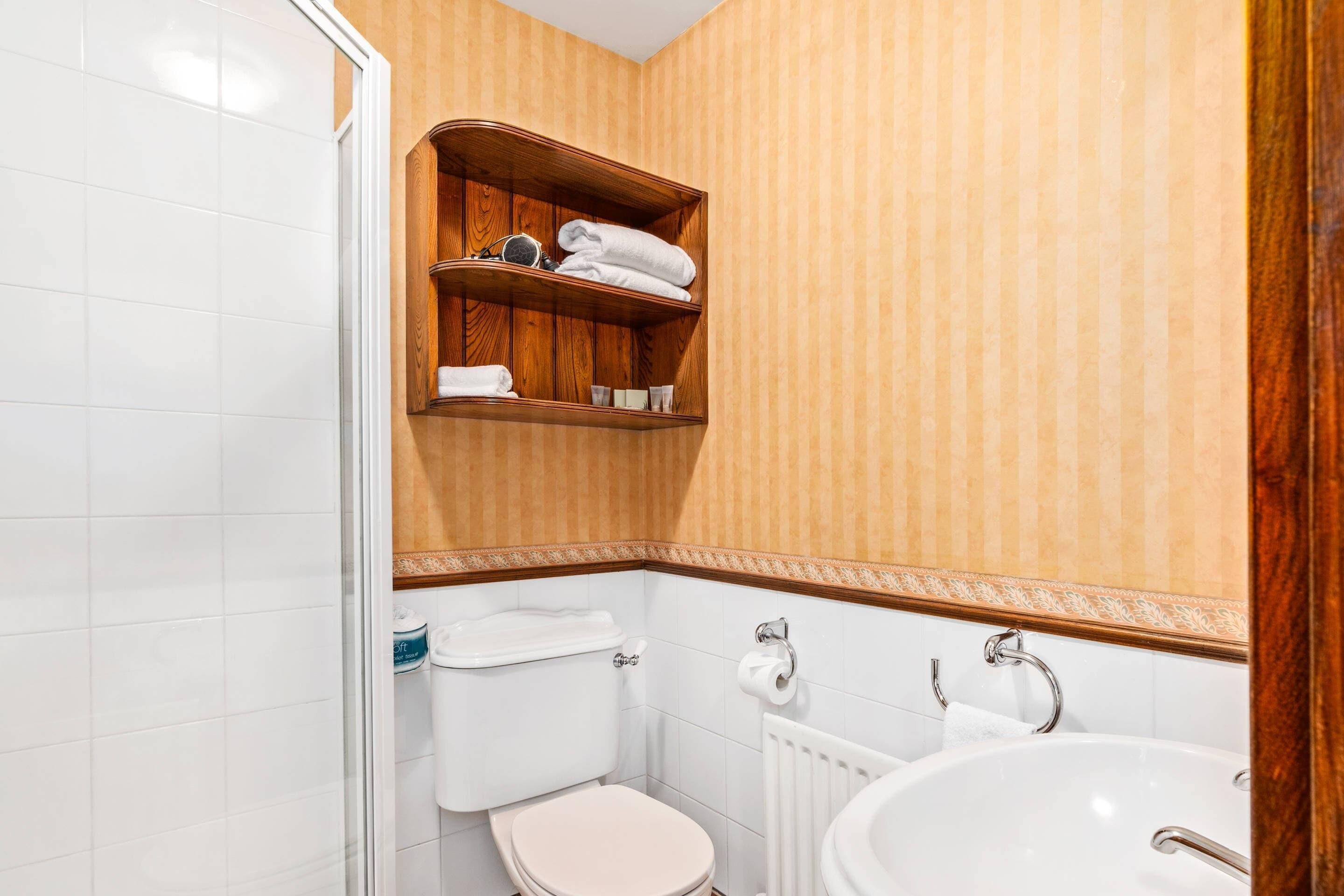 Ein Badezimmer mit Toilette, Waschbecken und einem Holzregal mit Handtüchern.