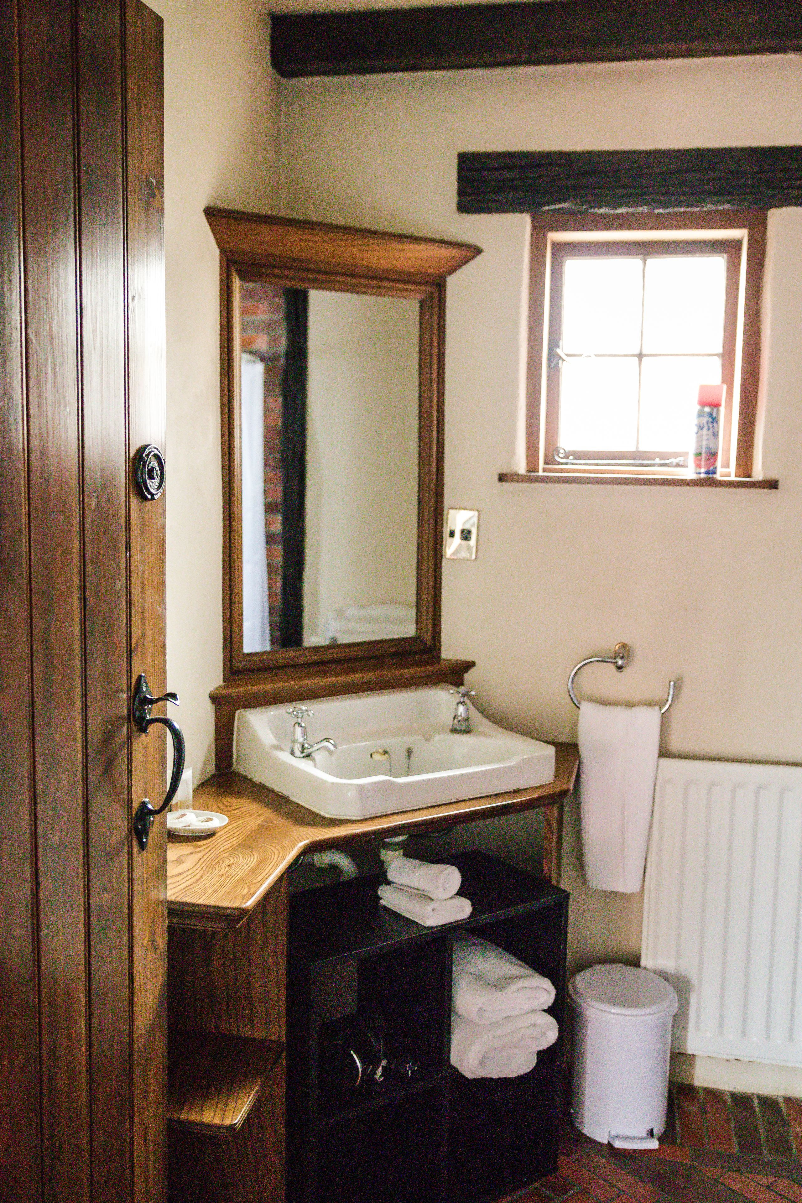 Un baño con tocador de madera, lavabo blanco, espejo, ventana y radiador.