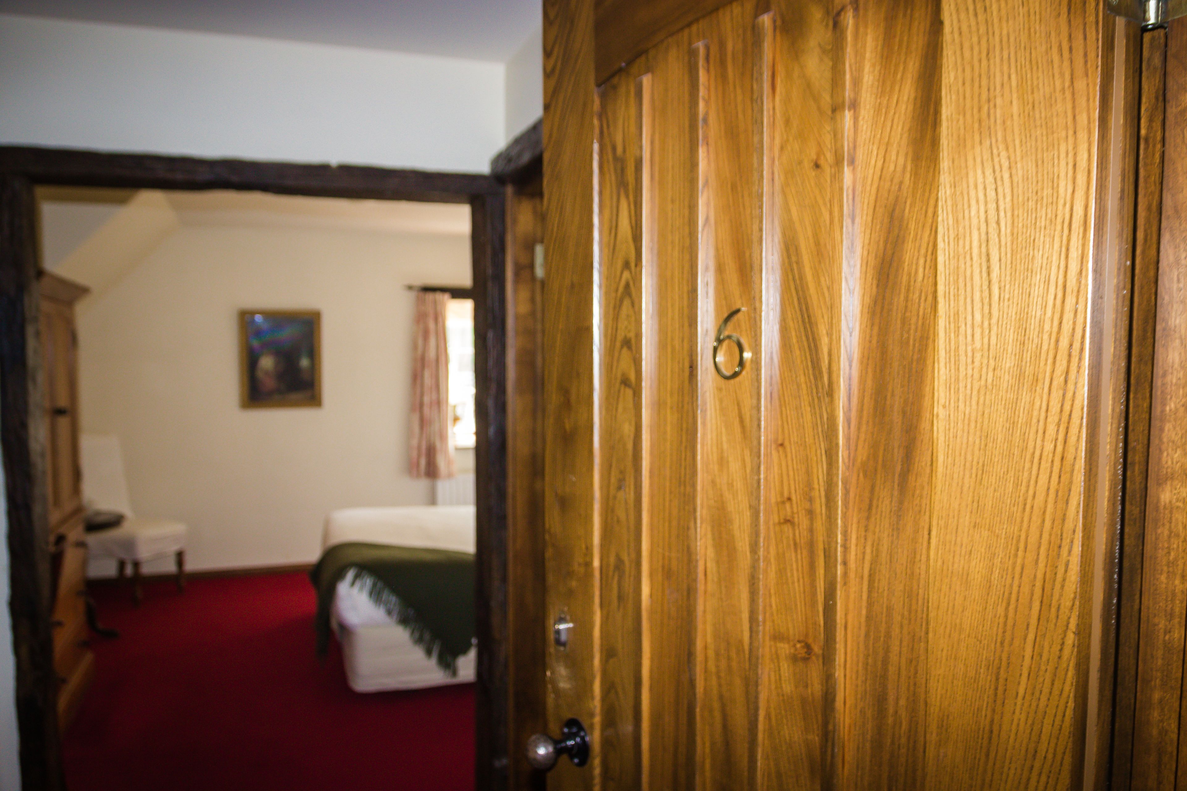 A room with a wooden door, a bed, a small table, and a chair.