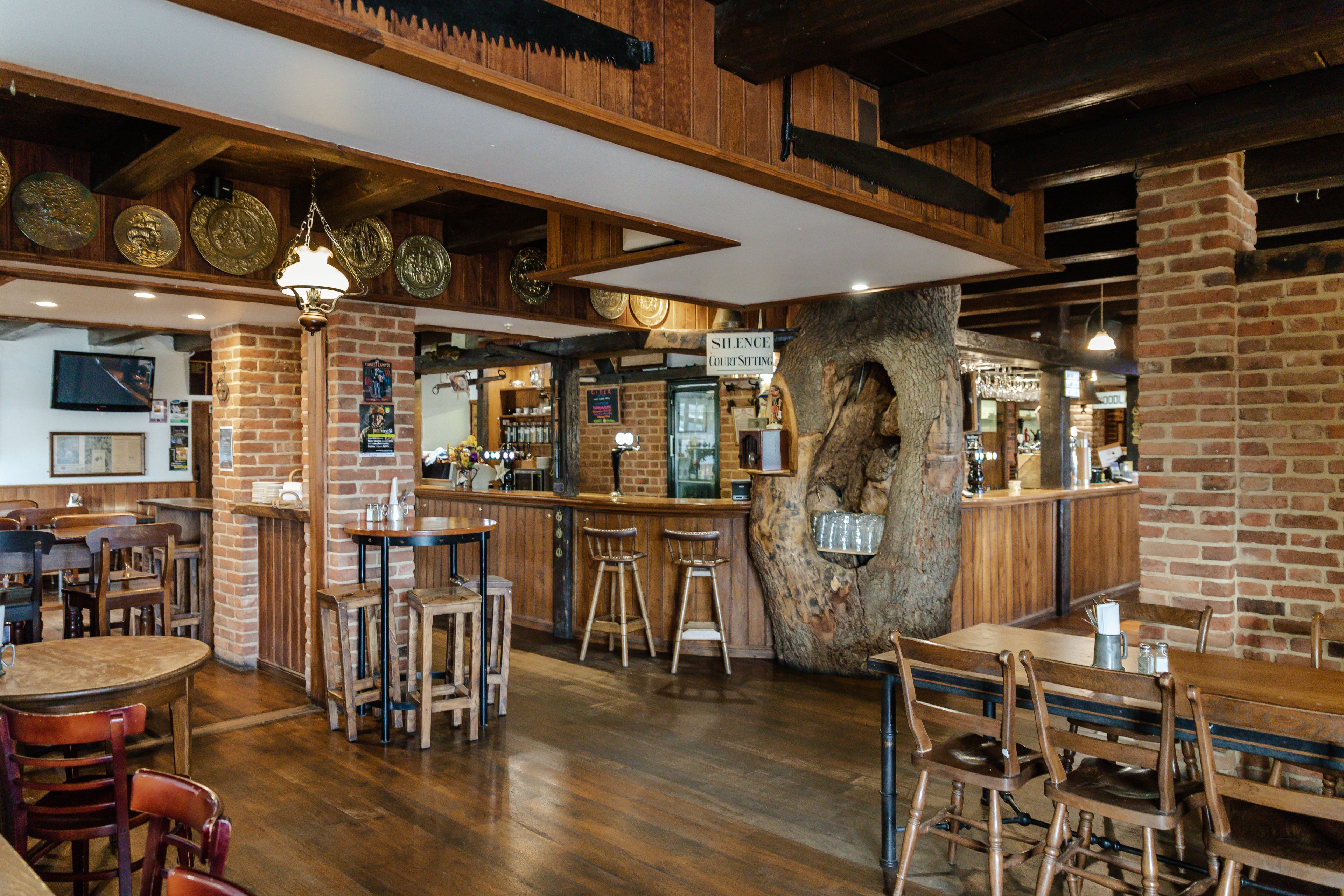 Interior de restaurante con mesas y sillas de madera, una zona de bar y una pared de ladrillo.