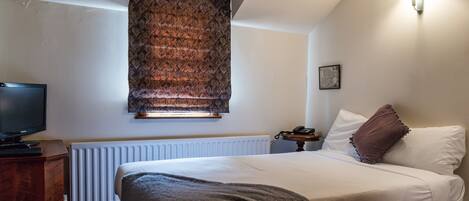 A bedroom with a bed, a television, a radiator, and a window with a patterned blind.