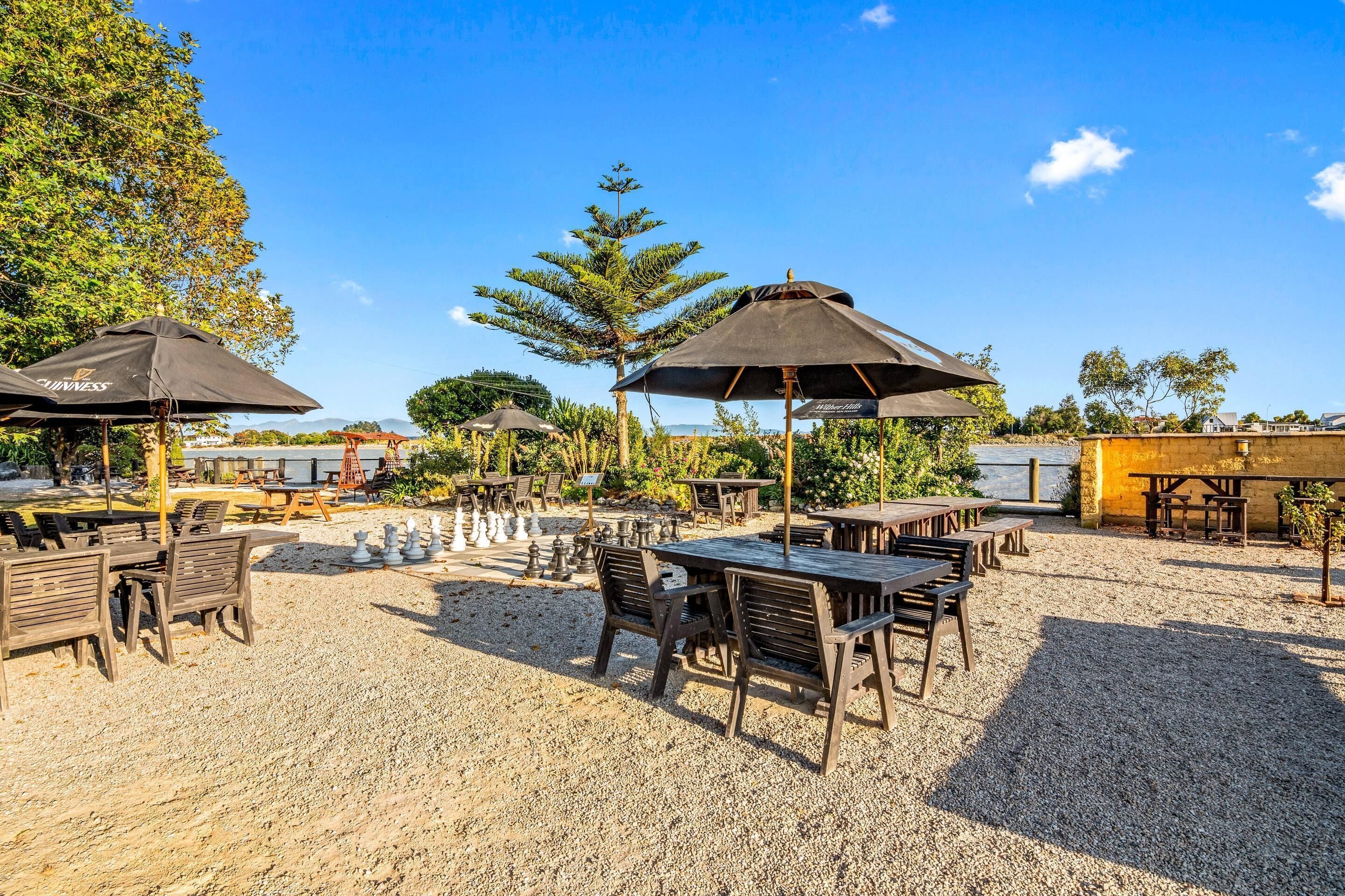 An outdoor seating area with tables and chairs, umbrellas, and a gravel ground.