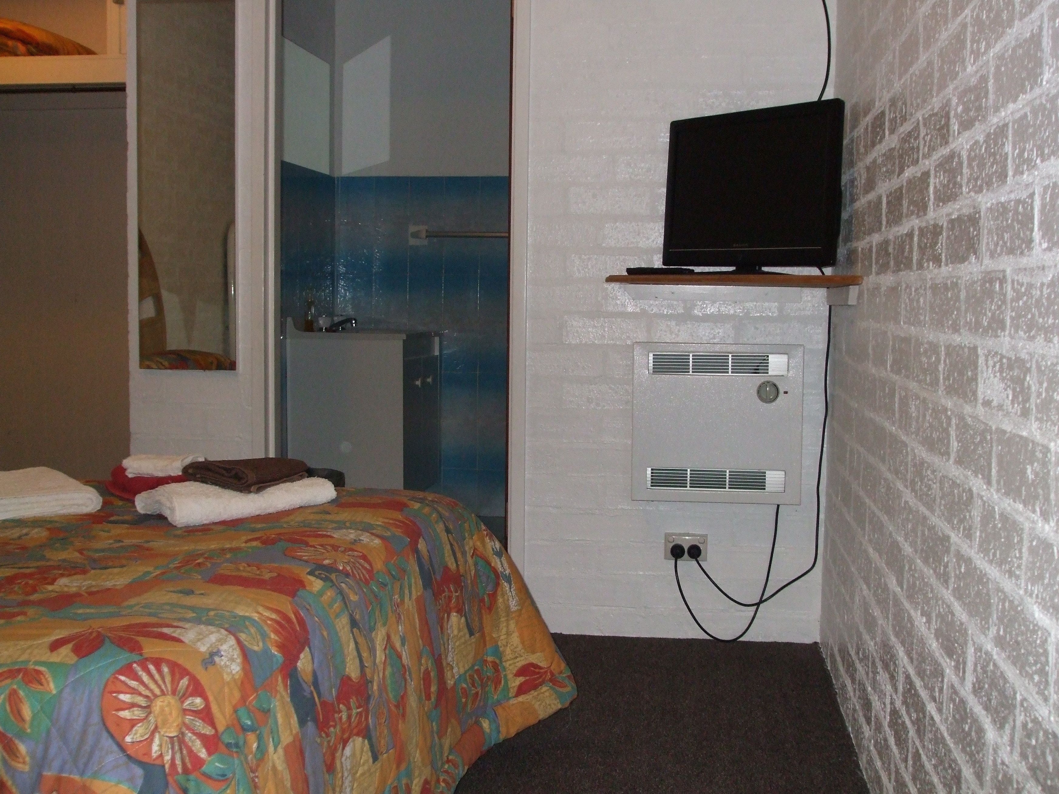 A hotel room with a bed, a television on a shelf, a shower, and a brick wall.