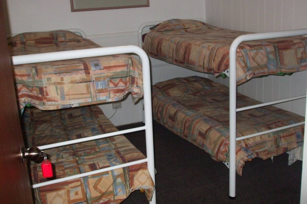 A bunk bed room with a patterned bedspread, a framed picture on the wall, and a door with a keychain.