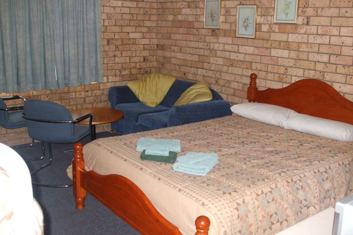 A hotel room with a brick wall, a bed with a wooden headboard, a blue sofa, a small round table, and a chair.