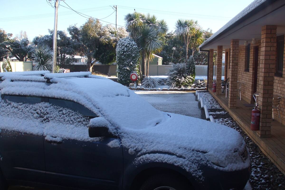 A car covered in snow parked in front of a building with a brick facade.