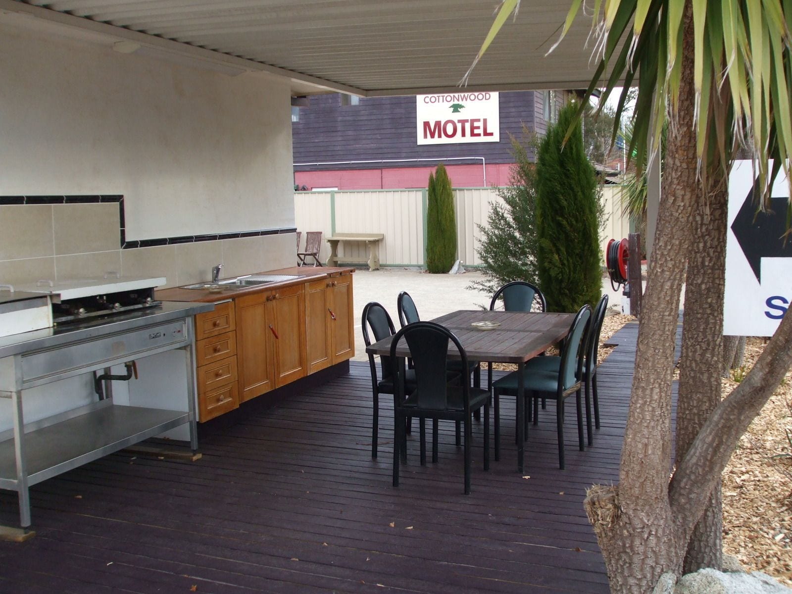 Un espace cuisine extérieur équipé d’un barbecue, d’une table à manger et de chaises. On peut apercevoir, au fond, une enseigne du Cottonwood Motel.