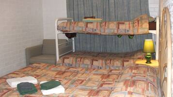 A bunk bed room with a patterned bedspread, a small bedside table with a lamp, and a chair.