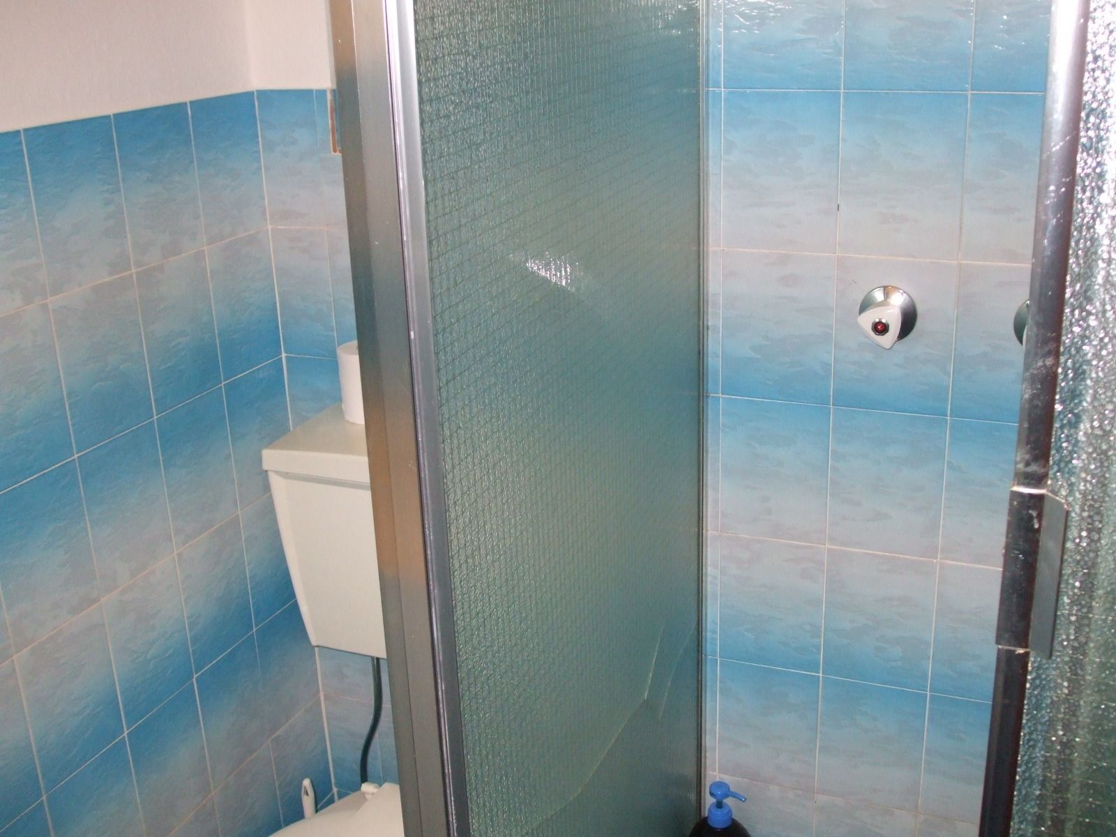 Un baño con azulejos azules, cabina de ducha de vidrio y un inodoro.