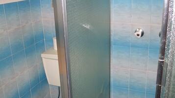 Un baño con azulejos azules, cabina de ducha de vidrio y un inodoro.