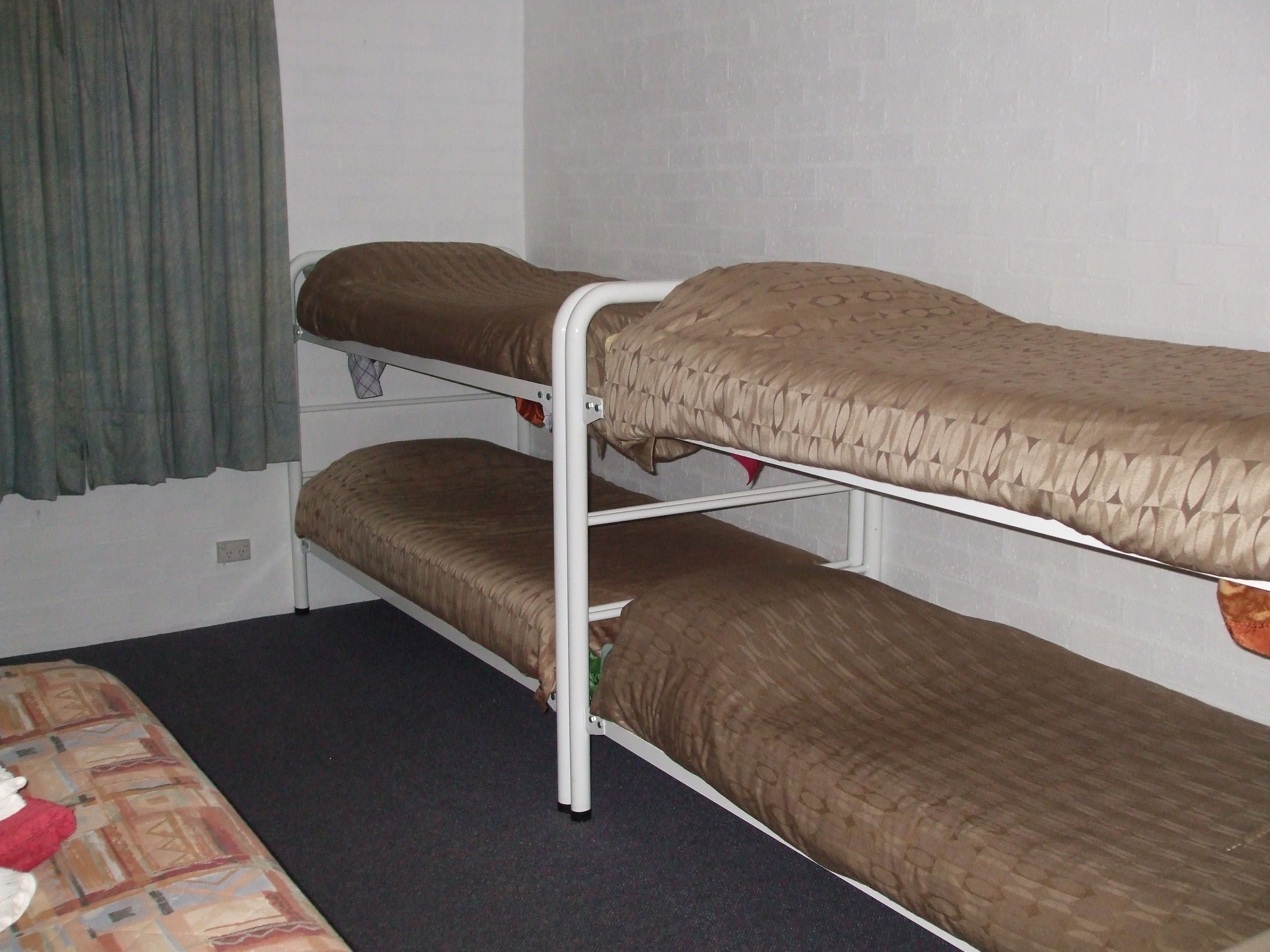 Ein Etagenbett mit zwei Schlafstellen, einem grünen Vorhang und einer gemusterten Bettdecke.