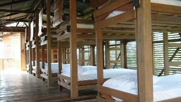 Varias literas de madera con ropa de cama blanca, bajo una estructura cubierta con piso de madera.