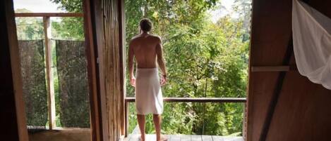 A man standing on a wooden deck with a view of lush greenery.