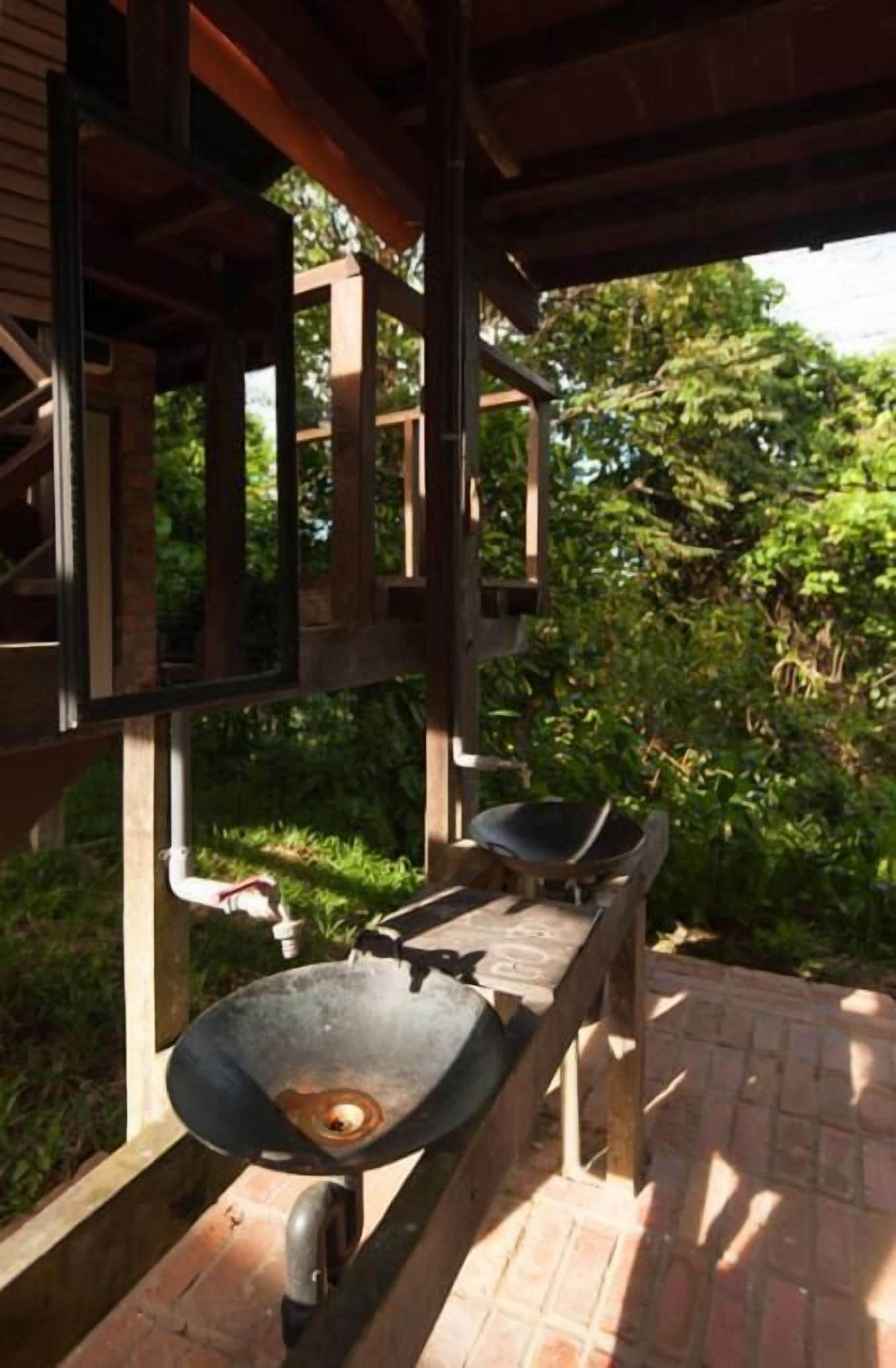 A rustic outdoor kitchen with a large wok, a sink, and a wooden bench.