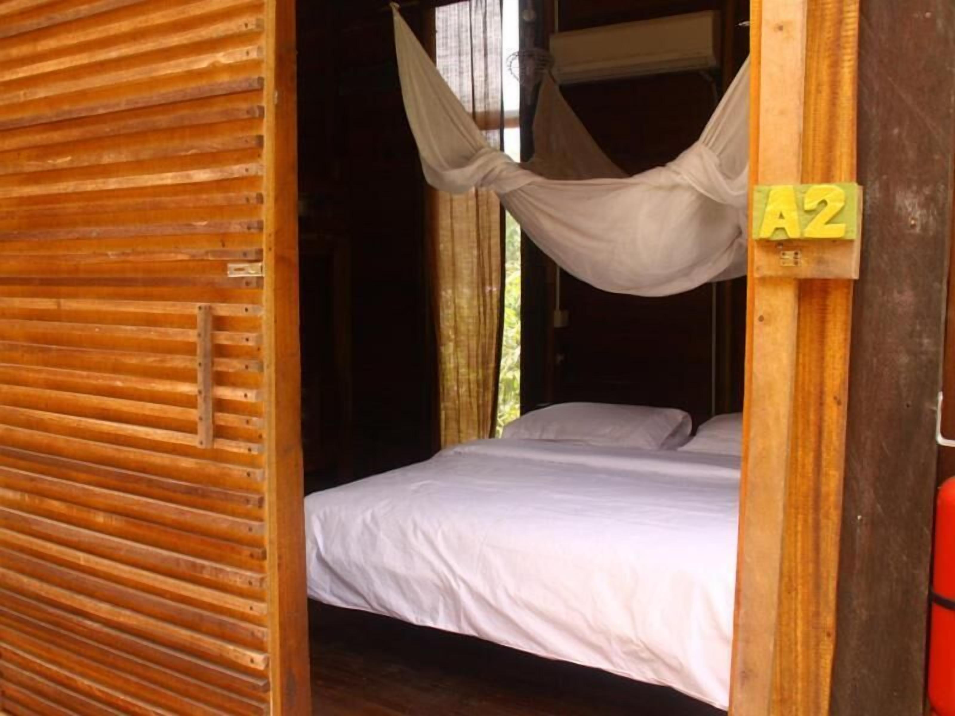 A single bed in a room with a wooden slatted door and a hanging mosquito net.