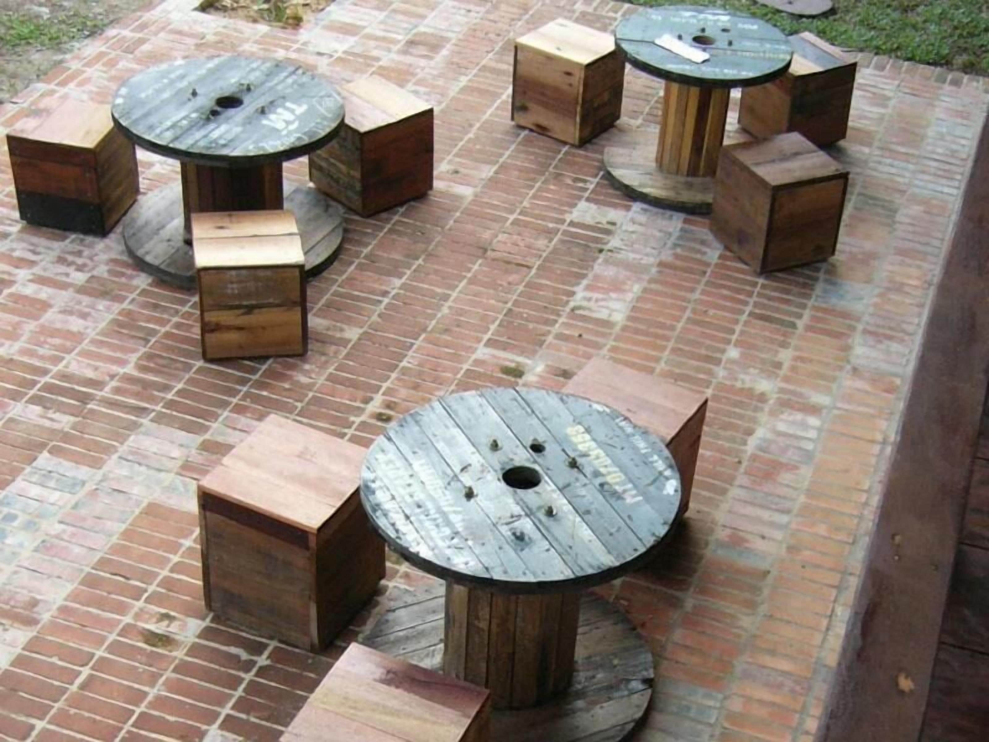 Mesas y bancos de madera al aire libre, dispuestos en un patio de ladrillo.
