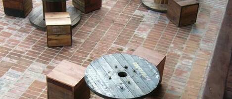Mesas y bancos de madera al aire libre, dispuestos en un patio de ladrillo.