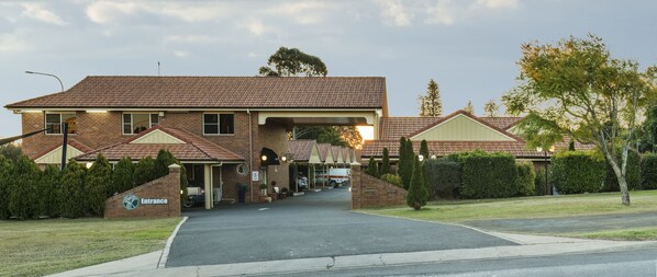 A brick building with a tiled roof, a covered entrance, and a parking area.