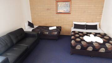 A hotel room with a brick wall, two single beds with patterned bedding, a black leather sofa, and a framed picture above the beds.