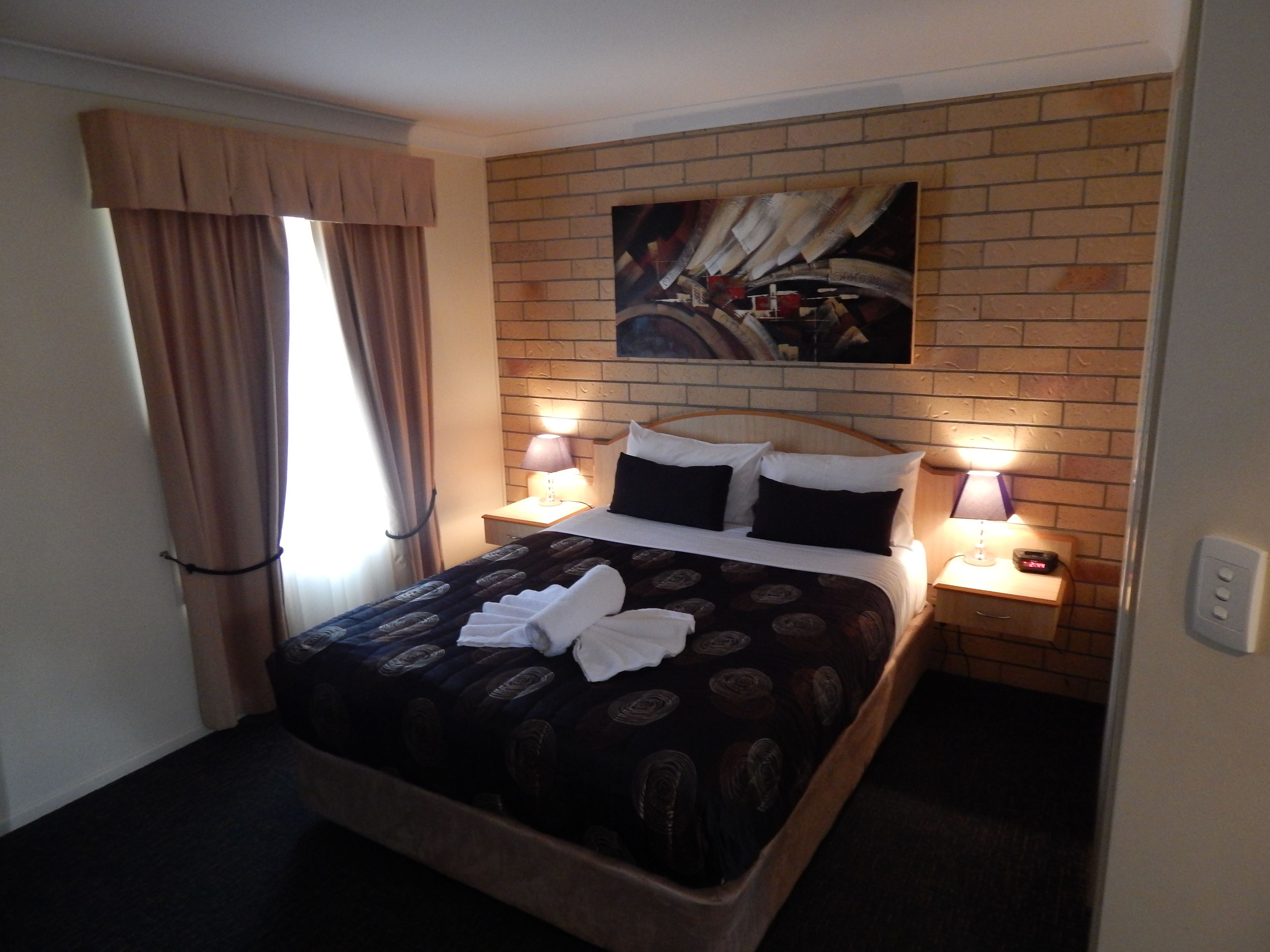 Habitación de hotel con una cama, dos lámparas de noche, un cuadro en la pared y una ventana con cortinas.