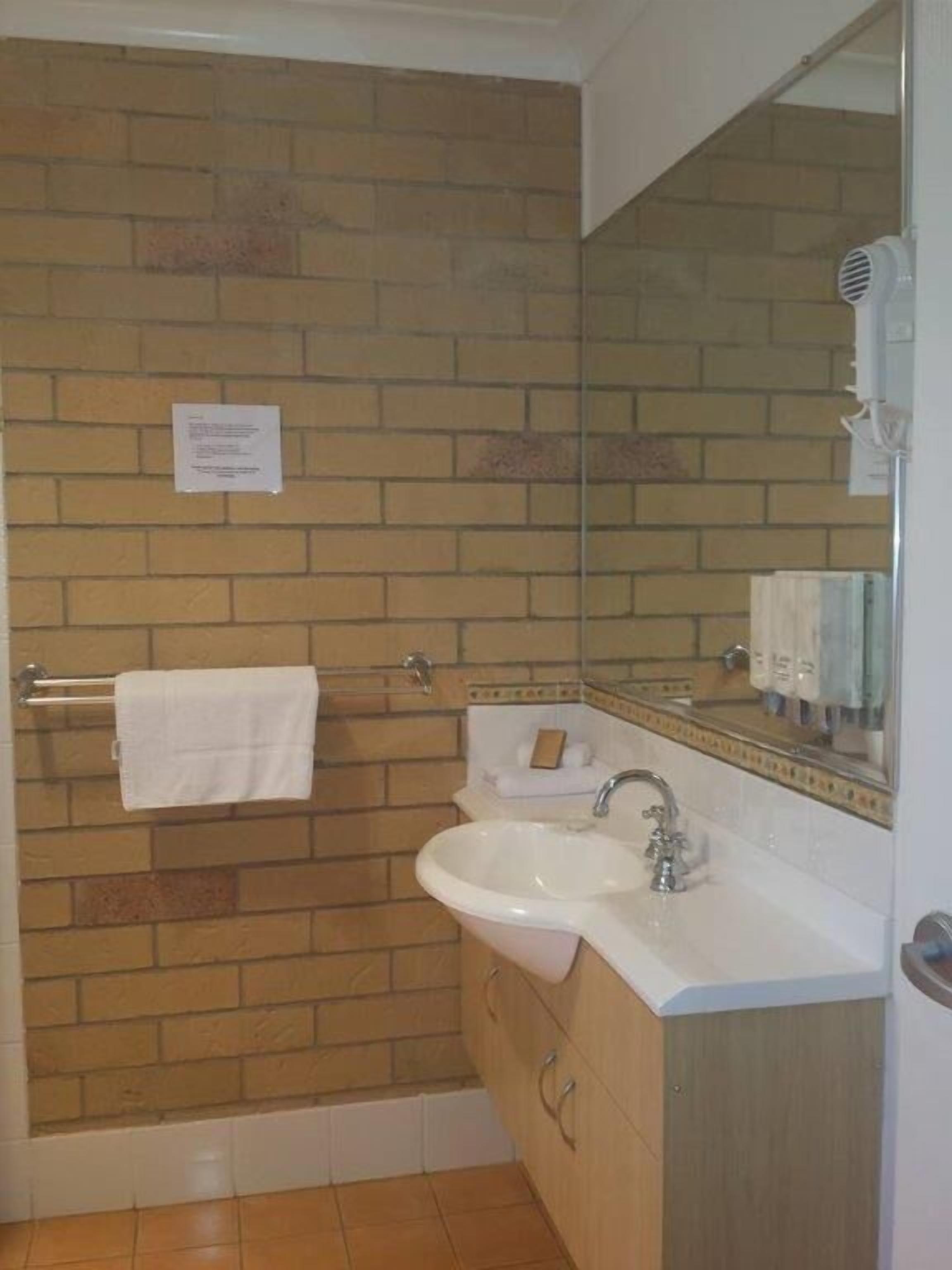 A bathroom with a brick wall, a white sink, a mirror, and a towel rack.