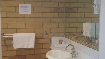 A bathroom with a brick wall, a white sink, a mirror, and a towel rack.