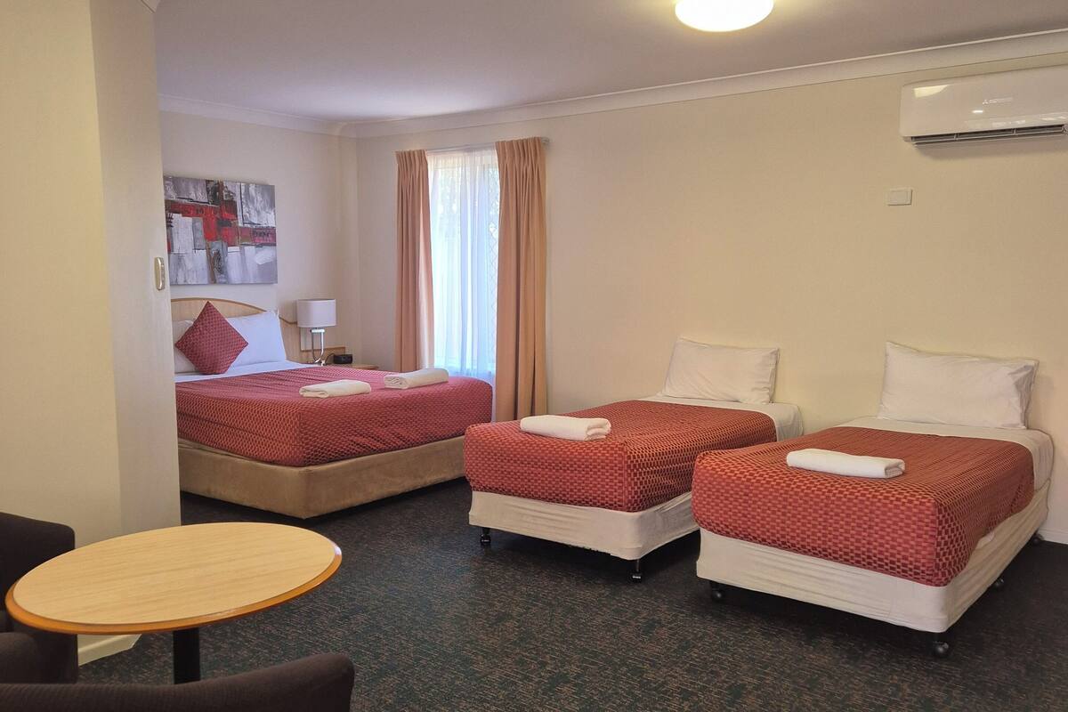 A hotel room with two beds, a small table, and a chair.