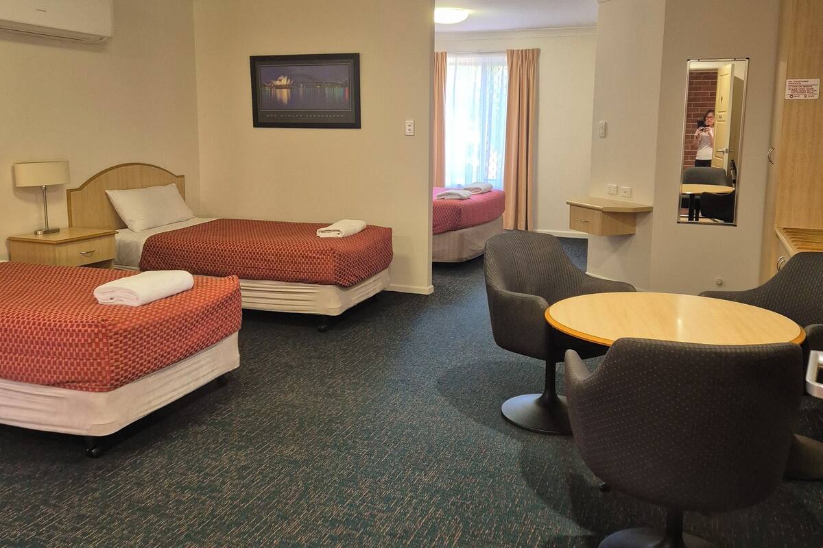 A hotel room with two beds, a small table, a chair, a TV, and a mirror.