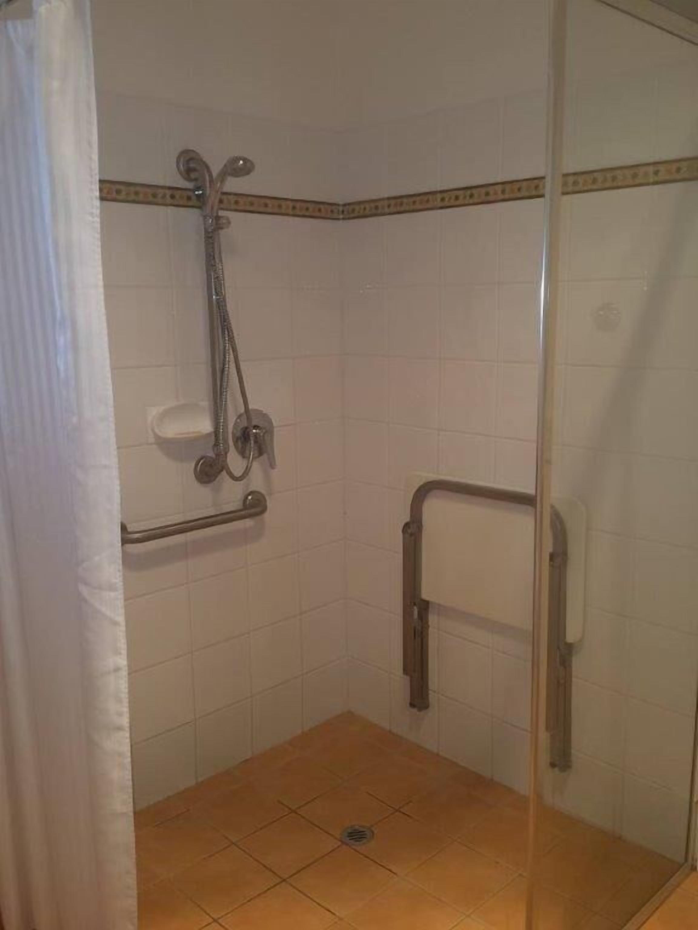 A small, enclosed shower area with a glass door, a handrail, and a tiled floor.