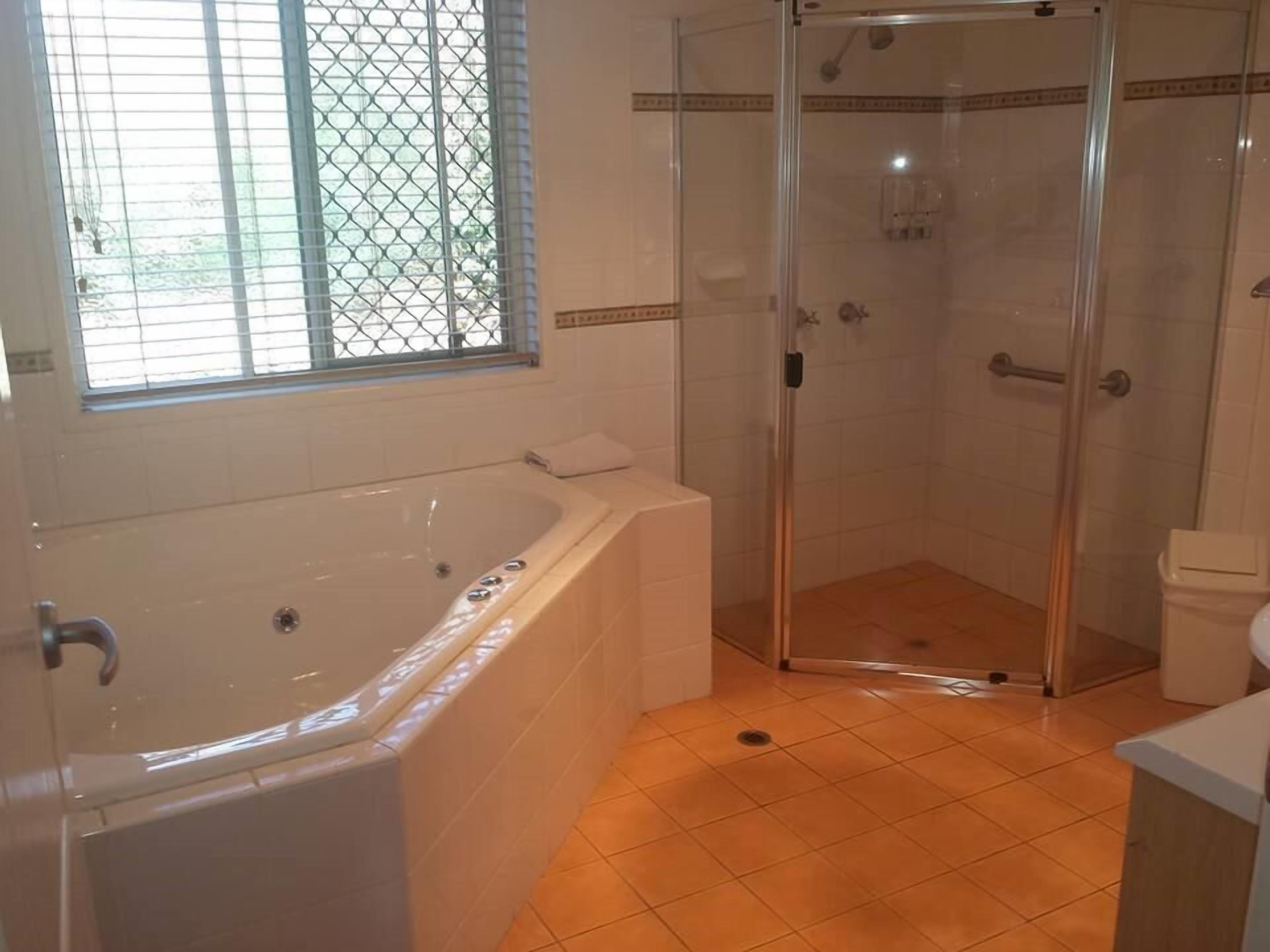 Une salle de bain avec une baignoire, une douche à parois de verre et une fenêtre avec des stores.
