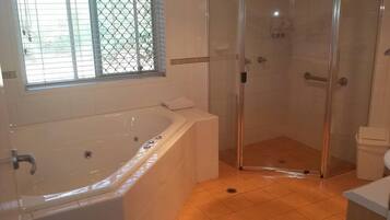 Une salle de bain avec une baignoire, une douche à parois de verre et une fenêtre avec des stores.