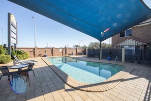 A swimming pool with lounge chairs and a shaded area, surrounded by a brick wall and a fence.