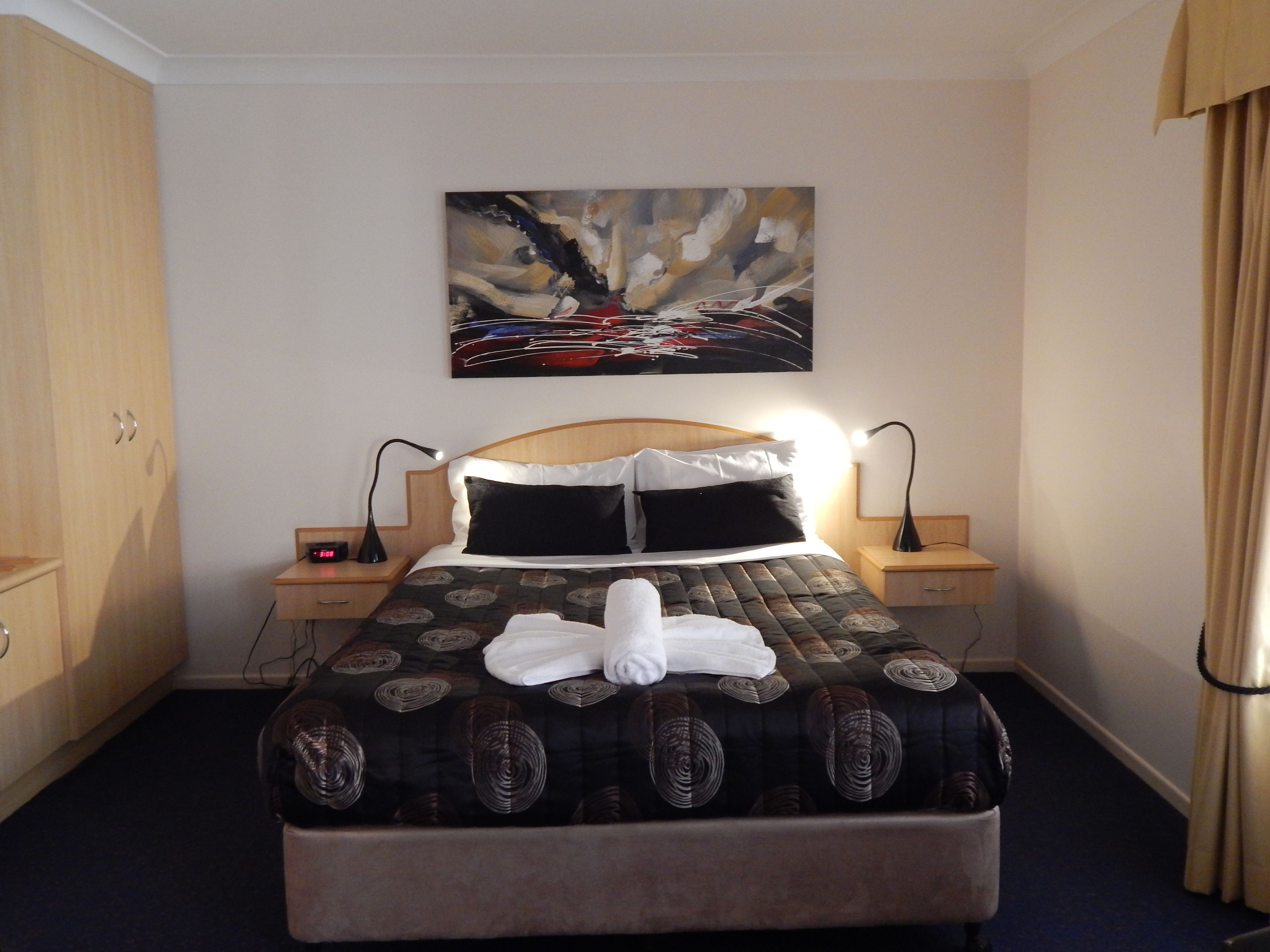 Un letto rifatto con una coperta a motivi, due abat-jour, una sveglia a parete e un quadro sopra il letto.