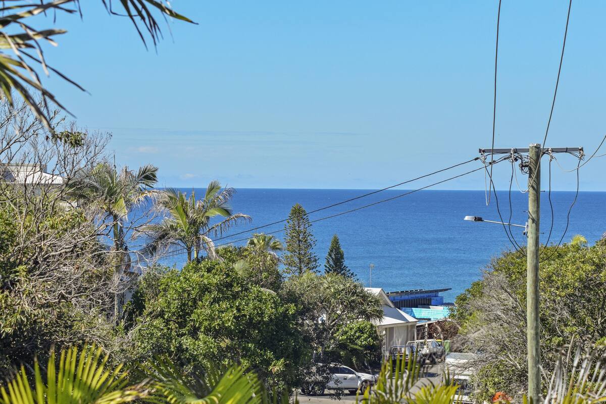 A coastal view with a clear sky, power lines, and a building with a blue roof.