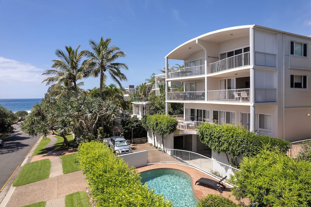 A multi-story hotel with a pool, surrounded by palm trees and a view of the ocean.