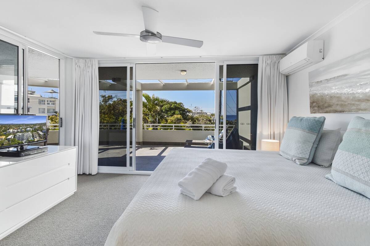 A modern hotel room with a large bed, a ceiling fan, a balcony with a view, and a TV on a dresser.