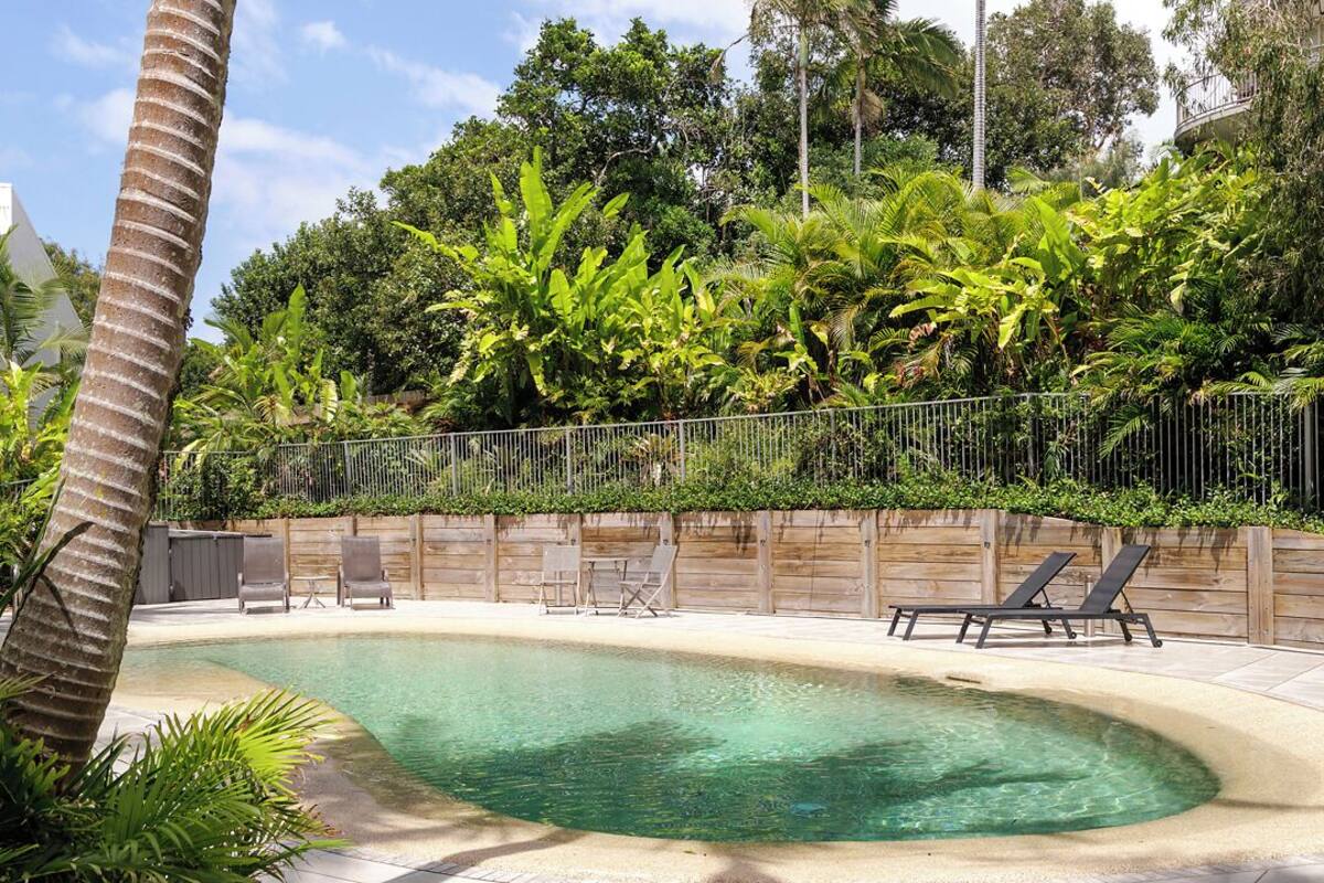 A swimming pool with lounge chairs and a wooden fence, surrounded by lush greenery.