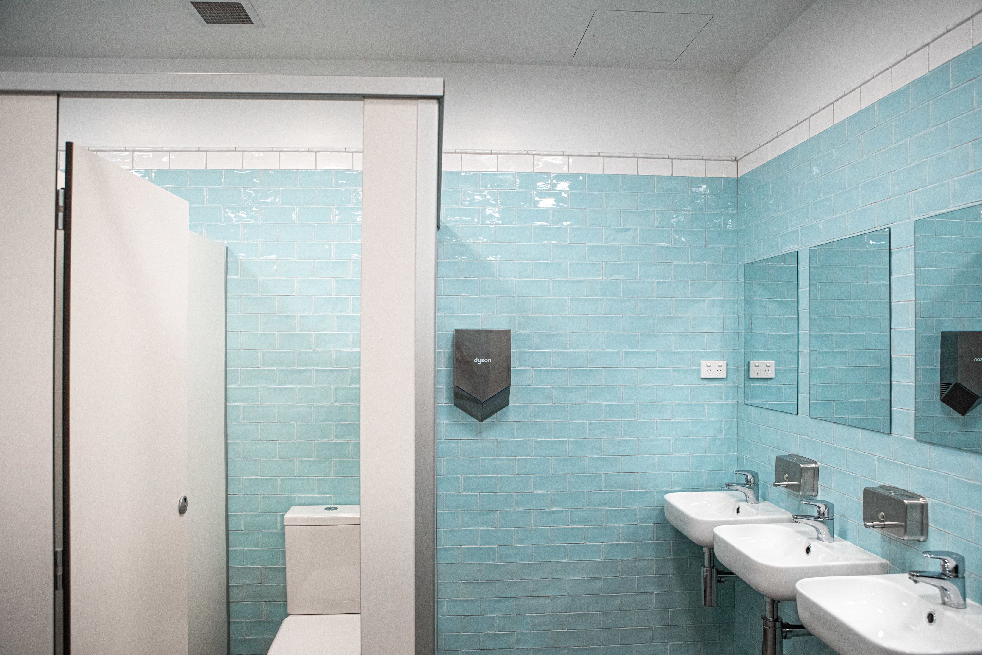 Une salle de bain avec des murs recouverts de carreaux bleus, des toilettes blanches et trois lavabos équipés de distributeurs de savon.