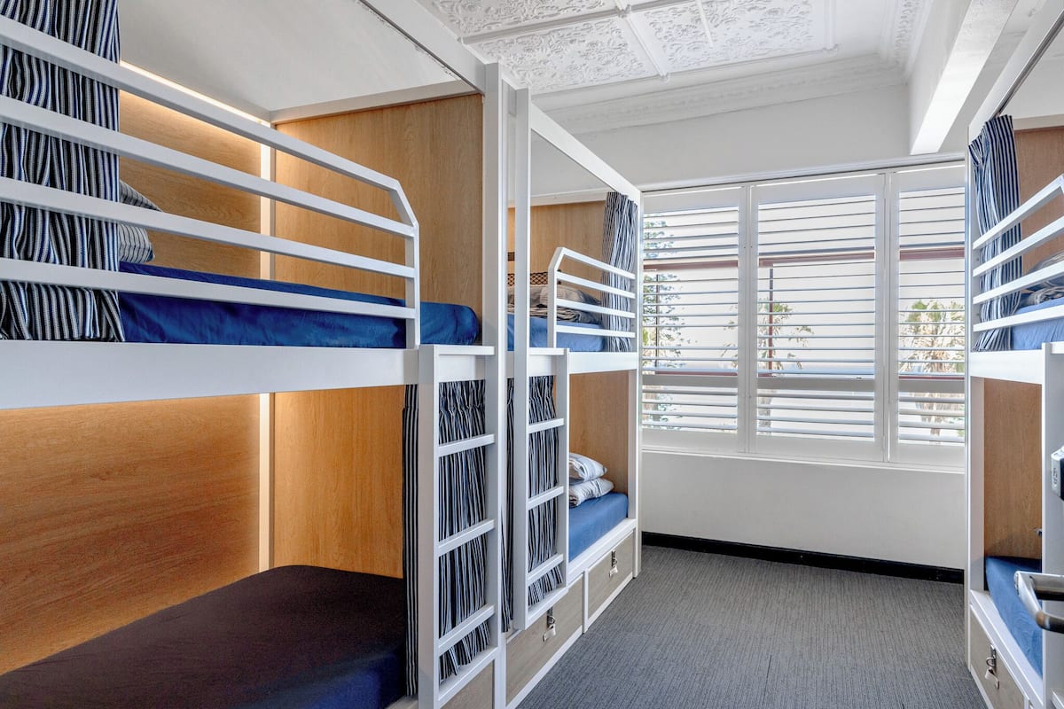 A bunk room with wooden headboards, a window with blinds, and a carpeted floor.
