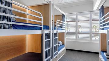 A bunk room with wooden headboards, a window with blinds, and a carpeted floor.