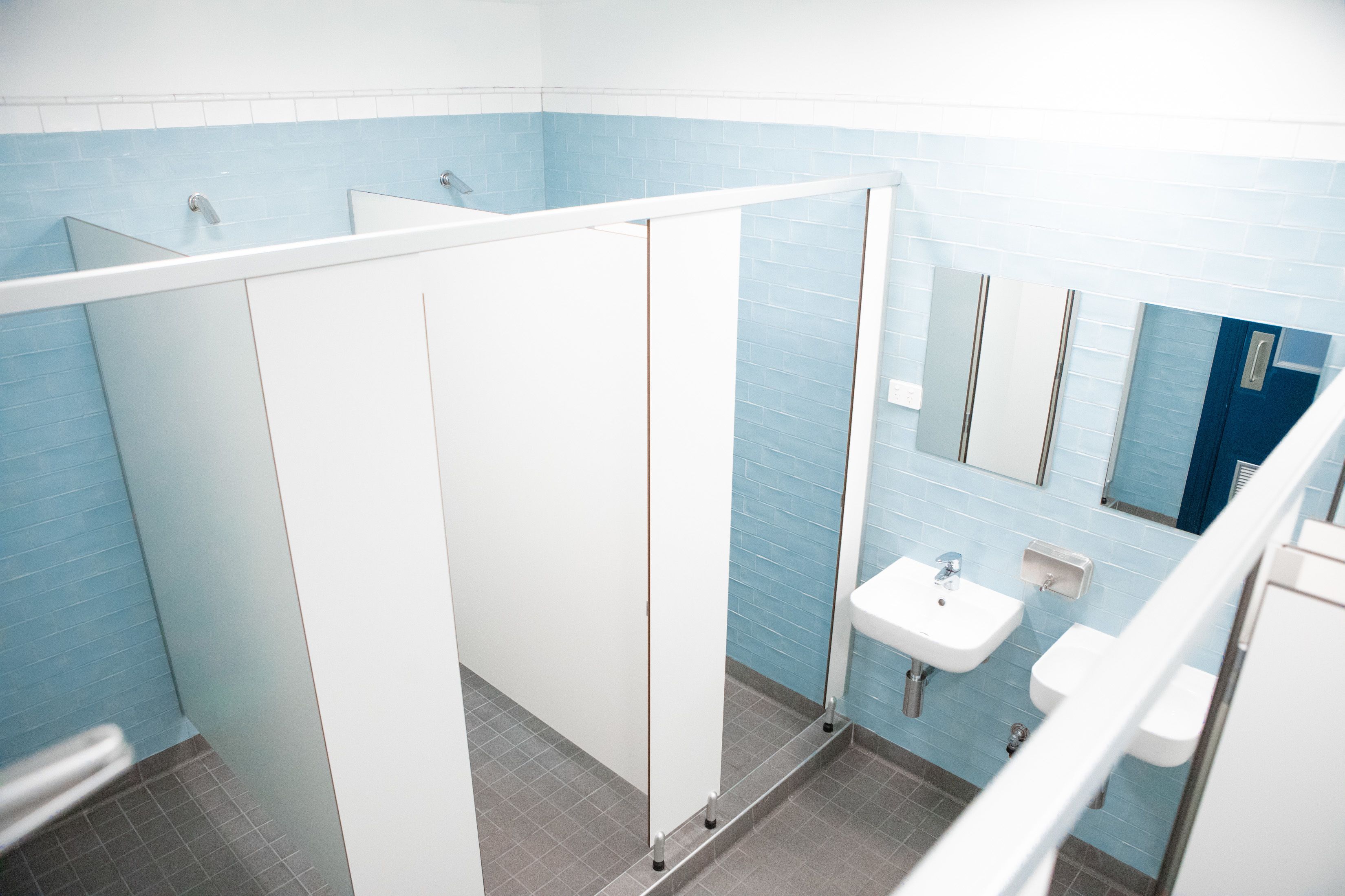 A bathroom with blue and white tiles, a sink, a mirror, and a partition.